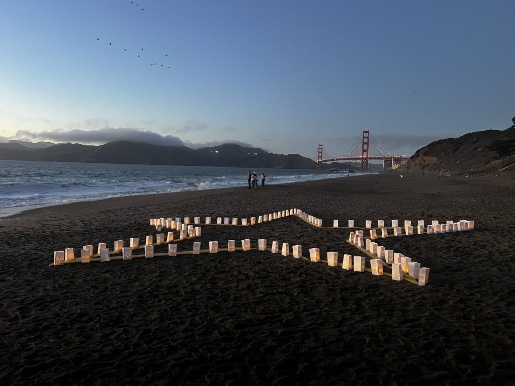 Candles arranged along the shoreline at dusk with the Golden Gate Bridge in the distance