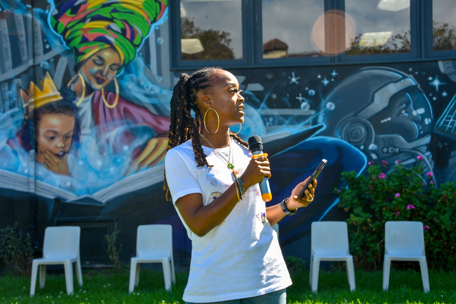 A speaker addressing families at the gathering, standing before a painted outdoor mural.
